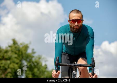 Homme dans des lunettes de soleil vitesse le long de la route sur un fond de parc d'été. Homme avec un vélo passe-temps manèges dans le parc. Banque D'Images