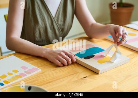 Mains de jeunes femmes créatives assises par table en bois dans l'atelier ou le studio et en utilisant le pochoir tout en créant de nouvelles peintures abstraites Banque D'Images