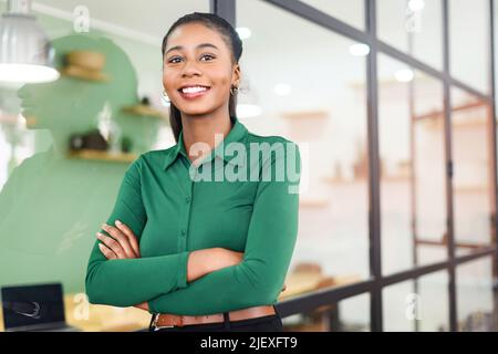 Portrait d'une femme d'affaires afro-américaine confiante debout avec les bras croisés, employée de bureau multiraciale déterminée dans une tenue élégante et décontractée, regardant l'appareil photo et souriant Banque D'Images