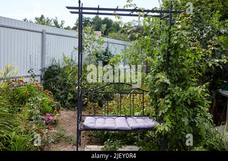 Aire de repos de jardin avec banc en métal entouré de fleurs et d'arbustes ornementaux. Place pour se reposer dans l'arrière-cour. Endroit confortable pour le week-end Banque D'Images