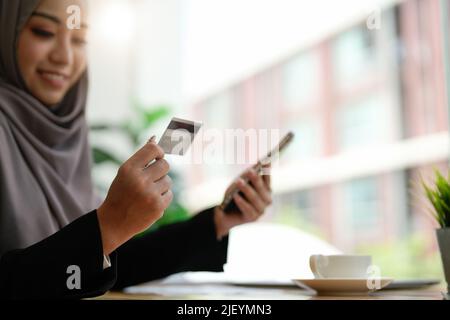 Gros plan asie musulmane dame utilisant le téléphone mobile, la carte de crédit acheter et d'acheter l'Internet de commerce électronique dans le bureau. Restez chez vous, faites vos achats en ligne, Banque D'Images