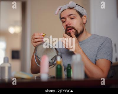 Concept de beauté pour hommes. Un homme de race blanche qui vérifie sa peau. Nutrition de la peau. Jeune homme appliquant du sérum organique essentiel sur le visage avec une pipette, espace libre Banque D'Images