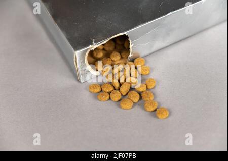 Une boîte rectangulaire argentée sur fond gris. La nourriture pour animaux déborde du trou. Aliments secs en pellicule. Nourriture pour animaux. Mise au point sélective. Banque D'Images