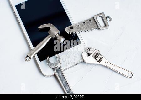 Téléphone portable avec un verre brisé et un ensemble d'outils à main essentiels sur une table en béton. Remplacement de l'écran du téléphone écrasé à la maison. Banque D'Images