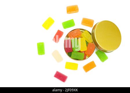 Boîte de bonbons avec cubes de gelée de fruits mélangés éparpillés sur fond blanc, vue du dessus. Banque D'Images