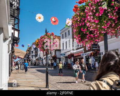 Guildford High Street, magasins et magasins, paniers de fleurs printanières et bannières saisonnières colorées au soleil bleu clair et chaud Guildford Surrey, Royaume-Uni Banque D'Images