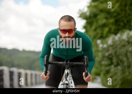 Homme dans des lunettes de soleil vitesse le long de la route sur un fond de parc d'été. Homme avec un vélo passe-temps manèges dans le parc. Banque D'Images