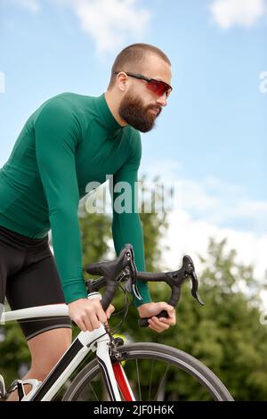 Homme dans des lunettes de soleil vitesse le long de la route sur un fond de parc d'été. Homme avec un vélo passe-temps manèges dans le parc. Banque D'Images