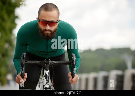 Homme dans des lunettes de soleil vitesse le long de la route sur un fond de parc d'été. Homme avec un vélo passe-temps manèges dans le parc. Banque D'Images