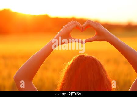 Gros plan d'une femme en forme de coeur dans un champ au coucher du soleil Banque D'Images