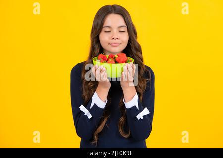 Enfant mangeant des fraises. Joyeux sourire enfant de l'adolescence tenir le bol de fraise sur fond jaune. Nourriture saine et naturelle en vitamines pour les enfants Banque D'Images