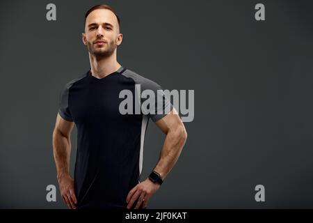 Portrait mi-long de jeune sportif dans un t-shirt et un short debout sur fond gris studio. Un sportif millénaire sérieux qui regarde la caméra Banque D'Images