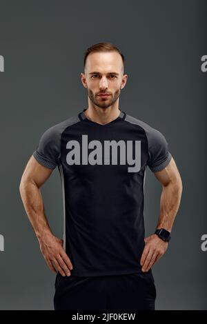 Portrait mi-long de jeune sportif dans un t-shirt et un short debout sur fond gris studio. Un sportif millénaire sérieux qui regarde la caméra Banque D'Images