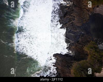 Vue de dessus de l'océan qui fait rage. Les vagues blanches mousseuse cassent sur une côte rocheuse inégale surcultivée avec de l'herbe verte. La beauté et la grandeur de la nature, des éléments Banque D'Images