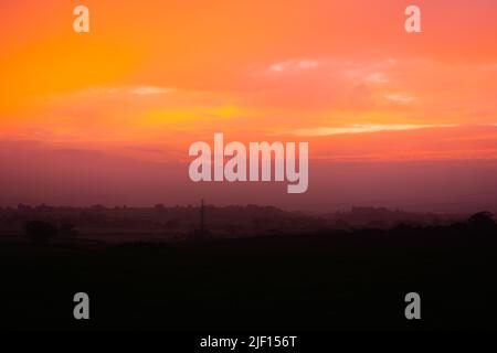 coucher de soleil orange pâle avec le soleil derrière les nuages et une ligne de quelques arbres en arrière-plan Banque D'Images