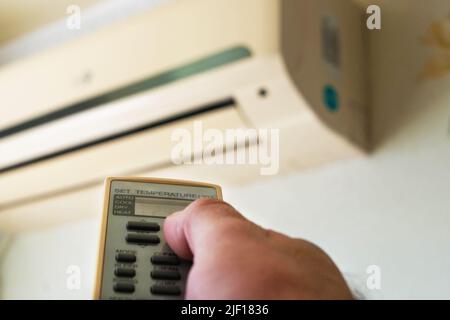 Un homme allume la climatisation à l'aide d'une télécommande pendant un été chaud Banque D'Images