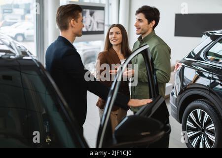 Joyeux jeune couple en consultant avec un vendeur d'automobiles, en choisissant une nouvelle voiture chez un concessionnaire automobile Banque D'Images