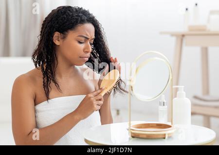 Femme noire mécontentait de peigner ses cheveux emmêlés avec la brosse Bamboo Banque D'Images