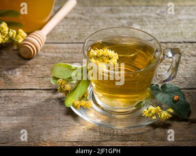 Un verre de thé de linden sur la table rustique. Fleurs de tilleul fraîches et fraîchement brassées. Banque D'Images