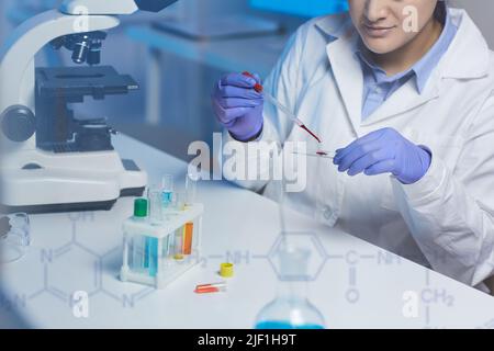 Gros plan d'un technicien de laboratoire concentré assis sur un bureau et en train de faire tomber du sang sur une lame de microscope tout en préparant l'échantillon pour le test Banque D'Images