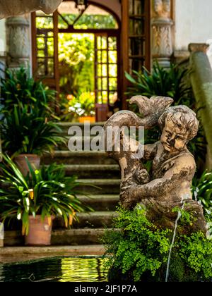 Portrait avec foyer sur une fontaine d'eau avec une sculpture d'enfant surcultivée avec de la mousse devant un escalier en pierre défoqué bordé de pots de plantes. Banque D'Images