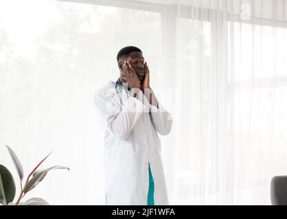 Un médecin afro-américain fatigué du travail dur est debout près de la fenêtre. Banque D'Images