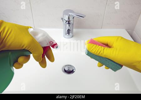 Les mains dans des gants de protection jaunes tiennent une éponge et un agent de nettoyage pour le nettoyage des équipements sanitaires dans la salle de bains Banque D'Images