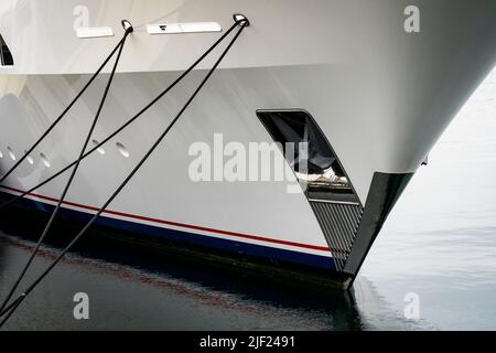 L'ancre sur l'arc d'un yacht de luxe flottant et réfléchissant sur l'eau douce tout en étant attaché le long d'un quai dans le port. Banque D'Images