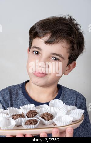 Enfant de 9 ans tenant un plateau avec des boules de fudge brésiliennes et faisant un visage douteux. Banque D'Images