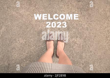 Vue de dessus des pieds de femme d'affaires avec des talons sur la route asphaltée et texte Bienvenue 2023. Concept de la nouvelle année 2023. Banque D'Images