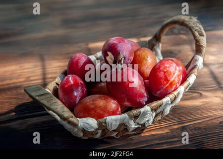 panier en osier rempli de prunes rouges sur une table rustique. photographié à la lumière naturelle dans la vie réelle. Banque D'Images