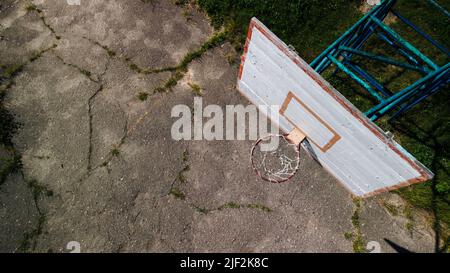 Ancien fond de panier de basket-ball. Fabriqué à partir de planches. Peinture écaillée et panier à brocher. Il y a un vieux asphalte fissuré sur le site. Vue d'en haut. Antenne Banque D'Images