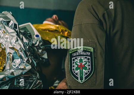 Le soldat est allongé sur une civière et est vérifié par le médecin . L'hôpital militaire de Pokrovskoe, dans la région de Dnepropetrovsk, stabilise les conditions des soldats blessés depuis les lignes de front. Ensuite, ils sont transférés dans les grands hôpitaux de Zaporizhia et Dnipro. Depuis le début de la guerre, les régions de Zaporizhia et de Dnipro ont fait l'objet d'attaques russes. Banque D'Images