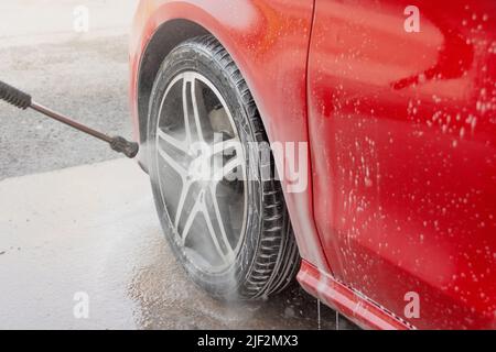 Lavage de voiture rouge dans un poste de lavage de voiture en libre-service. Cache-roue et pneu en caoutchouc. Lavage de voiture en libre-service Banque D'Images