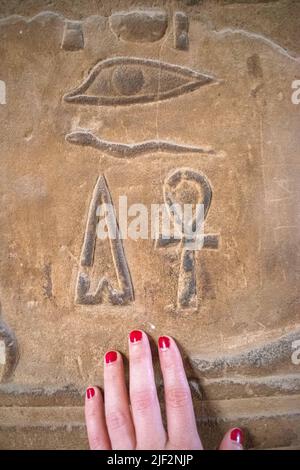 Main de femme aux ongles rouges, sur les reliefs et les hiéroglyphes égyptiens Banque D'Images