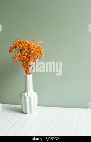 Vase de fleurs de gitsophila orange sur table blanche. Fond de mur vert kaki Banque D'Images