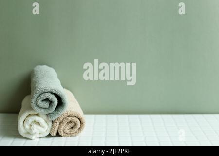 Serviette de bain sur table blanche. Fond de mur vert kaki. Concept de soins de la peau et spa Banque D'Images