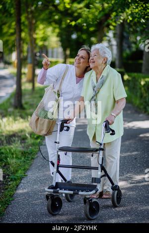 Soignant avec une femme âgée à pied avec une marchette dans le parc avec un sac à provisions. Banque D'Images