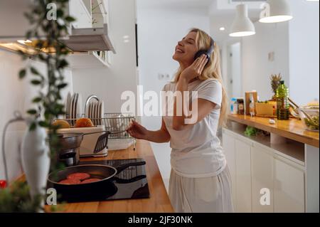 Jolie femme blonde gaie dans un casque pour faire des crêpes et écouter de la musique. Banque D'Images