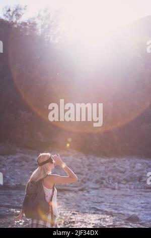 Femme qui vit la réalité virtuelle en utilisant un casque VR à côté d'une rivière pendant ses vacances. Femme en vacances portant un micro-casque VR Banque D'Images