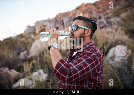 Un homme barbu boit de l'eau à partir d'une bouteille de verre tout en faisant de la randonnée dans les montagnes Banque D'Images