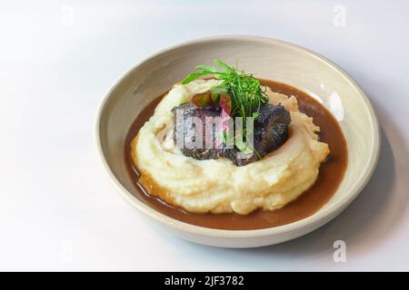 Poireaux de bœuf traditionnels sur purée de pommes de terre avec sauce au vin rouge brun et garnir de feuilles d'herbes sauvages dans un bol rustique sur une table légère, espace de copie, selec Banque D'Images