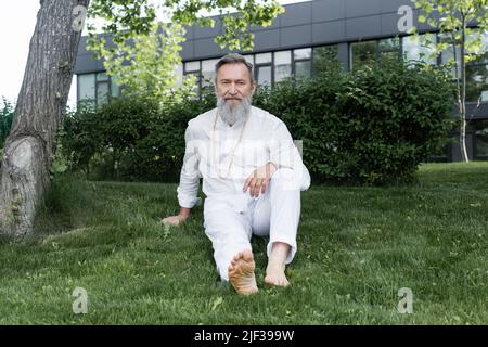 pleine longueur de gourou pieds nus en vêtements blancs assis sur l'herbe verte Banque D'Images
