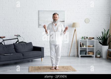 long gourou de yoga dans des vêtements blancs debout avec des pierres de selenite à la maison Banque D'Images