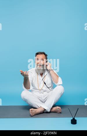 entraîneur de yoga dans le casque, assis en position facile sur le tapis de yoga et pointant avec la main sur le bleu Banque D'Images