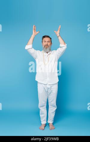 maître de yoga sur toute la longueur méditant avec des mains levées blanches debout sur bleu Banque D'Images