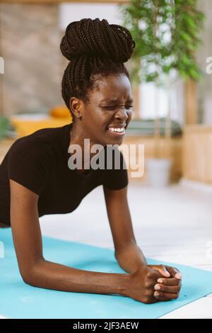 Durable et tenue sur la forme afro femme américaine debout dans le coude de la planche de gros plan, l'entraînement sur le tapis de gymnastique dans le studio décoré. Renforcement musculaire Banque D'Images