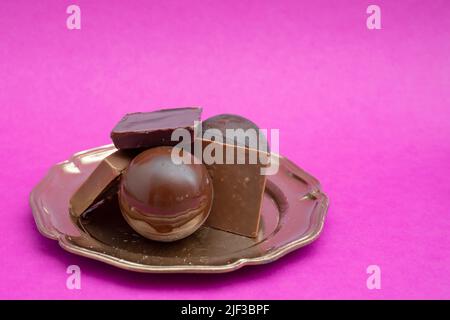 Boules de chocolat noir et carrés empilés sur un plateau doré, isolés sur fond fuchsia coloré. Banque D'Images