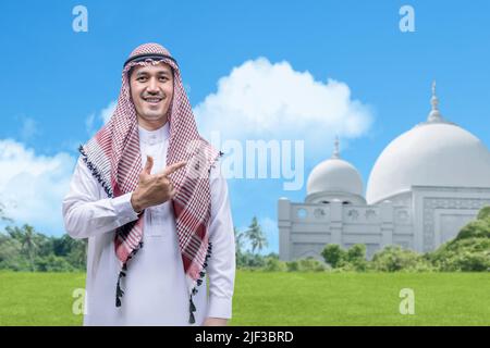 Homme arabe portant le keffiyeh debout avec une mosquée et un fond bleu ciel Banque D'Images