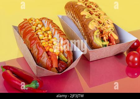 Hot dog avec saucisse dans une boîte en papier avec tomates et maïs, piments, concombre et laitue. Sur fond rouge. Restauration rapide. Espace de copie Banque D'Images